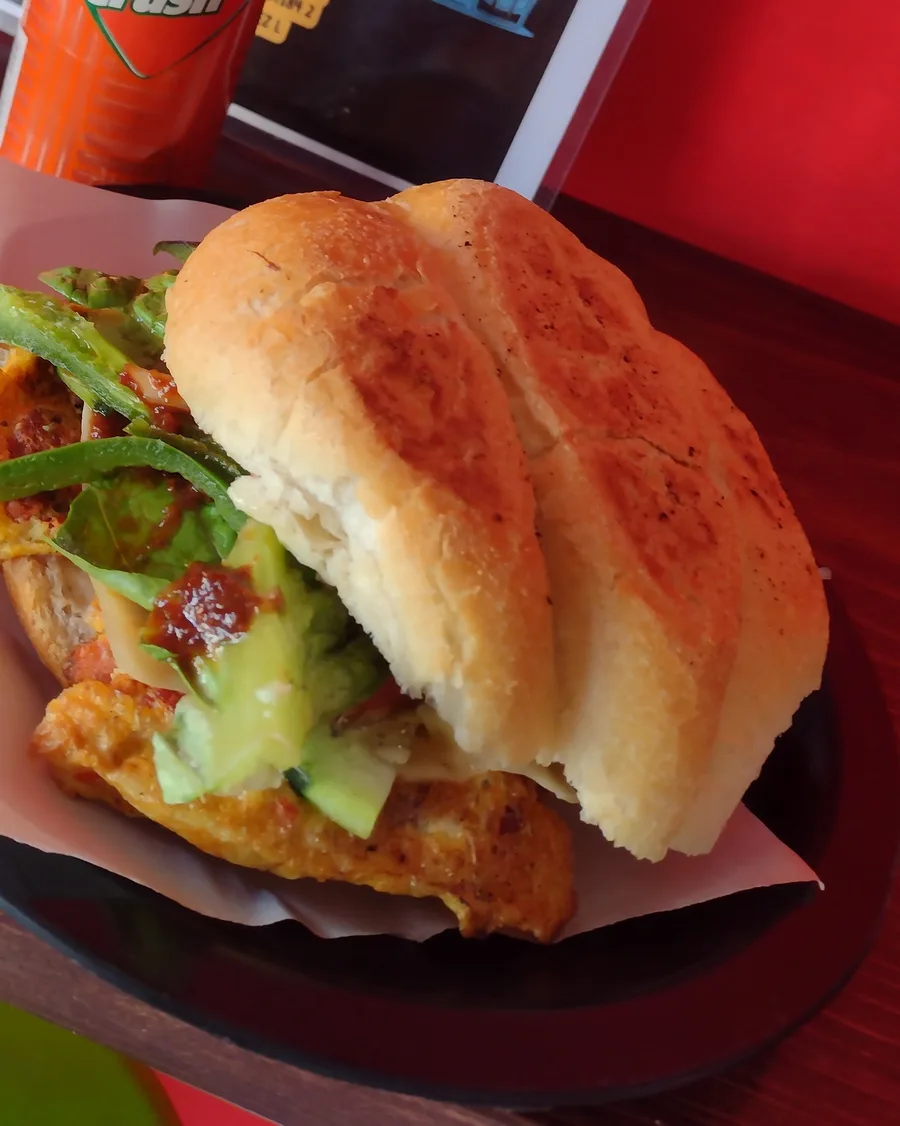 Torta en telera con rajas, aguacate y salsa roja, servida en charola